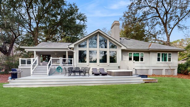 A house with a covered patio, outdoor seating, and a large window. - Beautiful half acre estate home with private hot tub and passes to the shared pool (Hilton Head)
