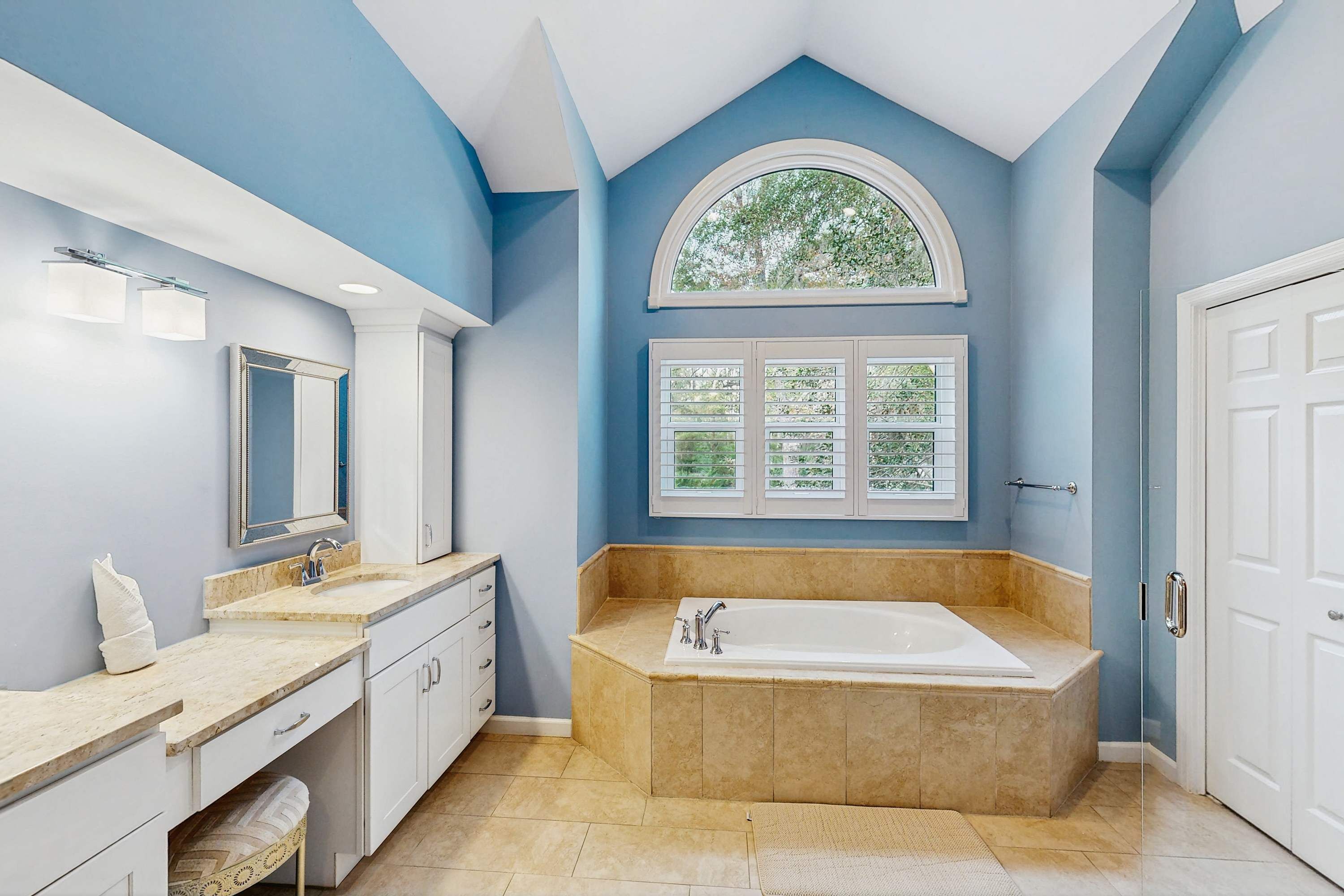 A bathroom with a bathtub, vanity, and a window with a view of greenery.