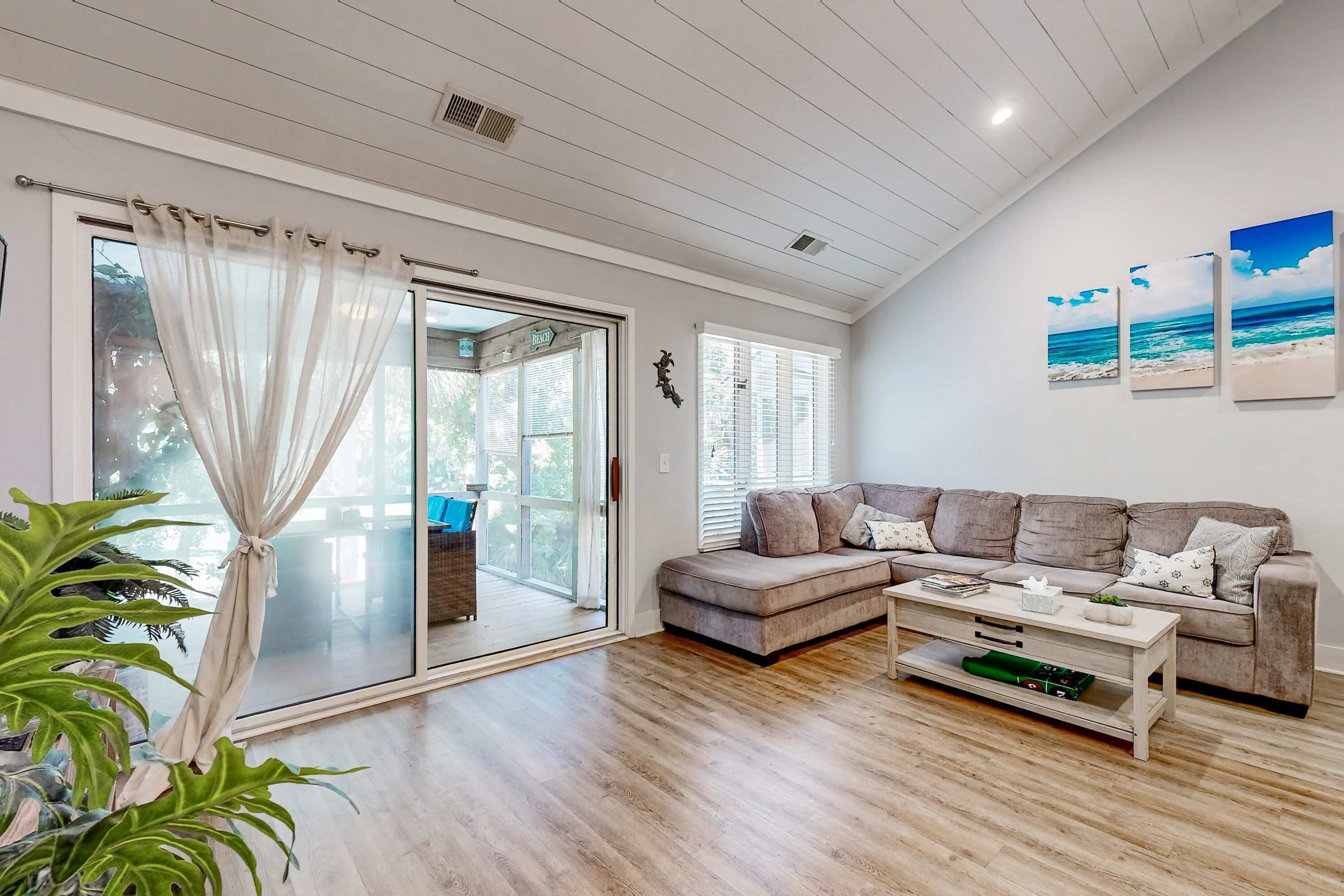Sala de estar com porta de vidro deslizante, sofá cinza, mesa de centro e uma planta.