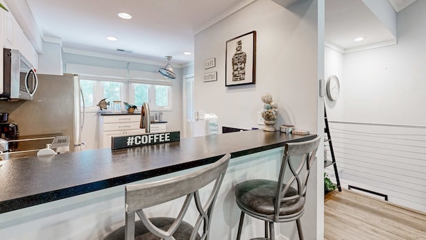 Une cuisine moderne avec un coin bar, des tabourets de bar, un panneau indiquant qu'il y a du café, et une horloge fixée au mur.