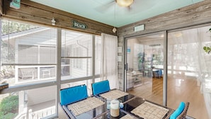 Une pièce avec un mur en verre, une table avec des coussins bleus et un ventilateur de plafond.