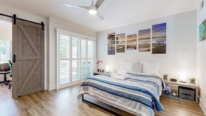 Une chambre à coucher comprenant un lit, un ventilateur de plafond, une porte coulissante et une fenêtre avec des stores.