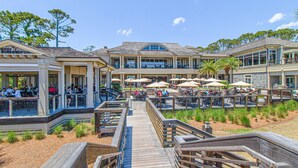 A beachfront hotel with outdoor dining areas, a wooden boardwalk, and multiple levels of balconies. - Coastal charmer villa with cove front balcony & trolley  walk to beach (Hilton Head)