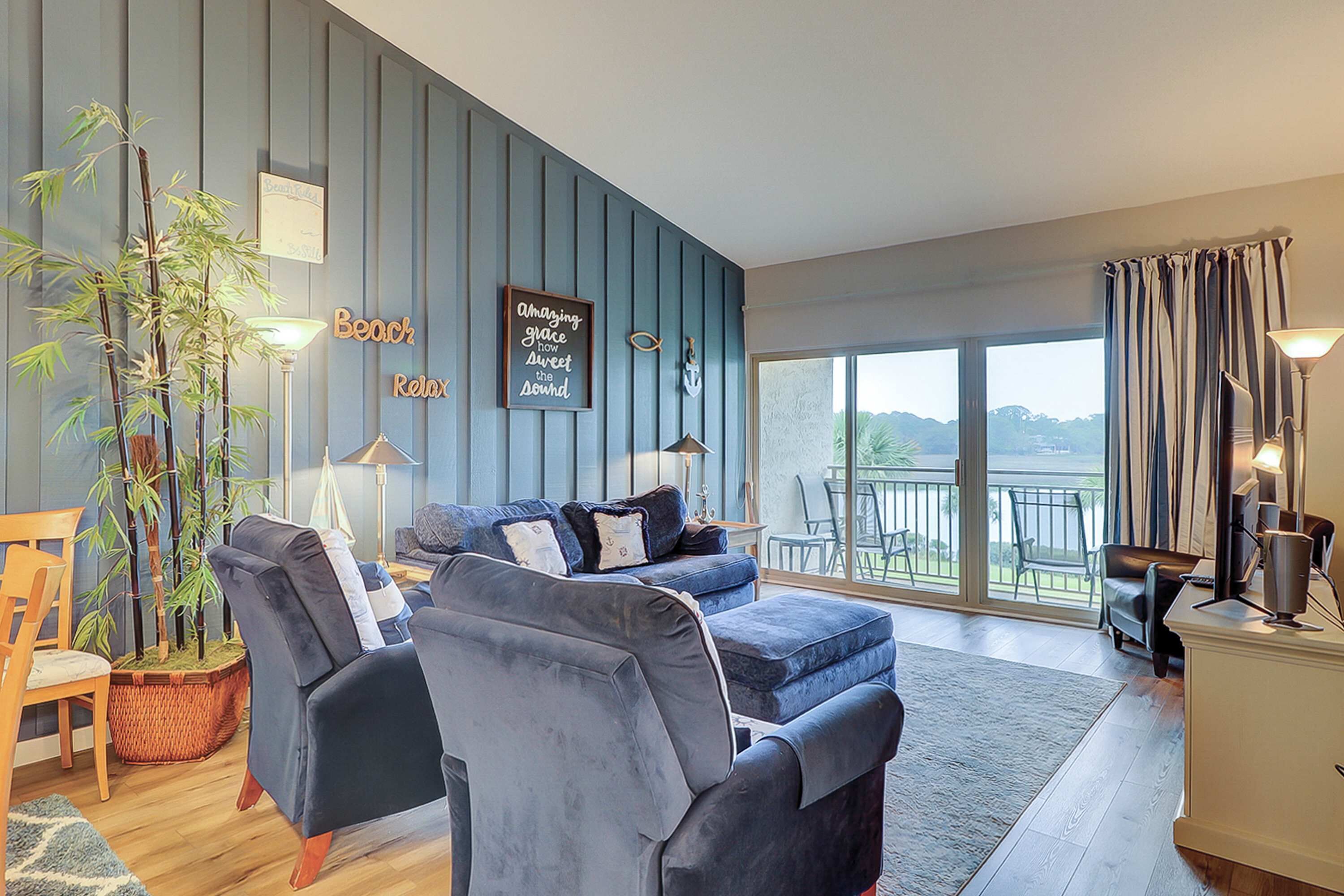 A modern living room with a blue wall, a sofa, a chair, a lamp, and a large window with a view.