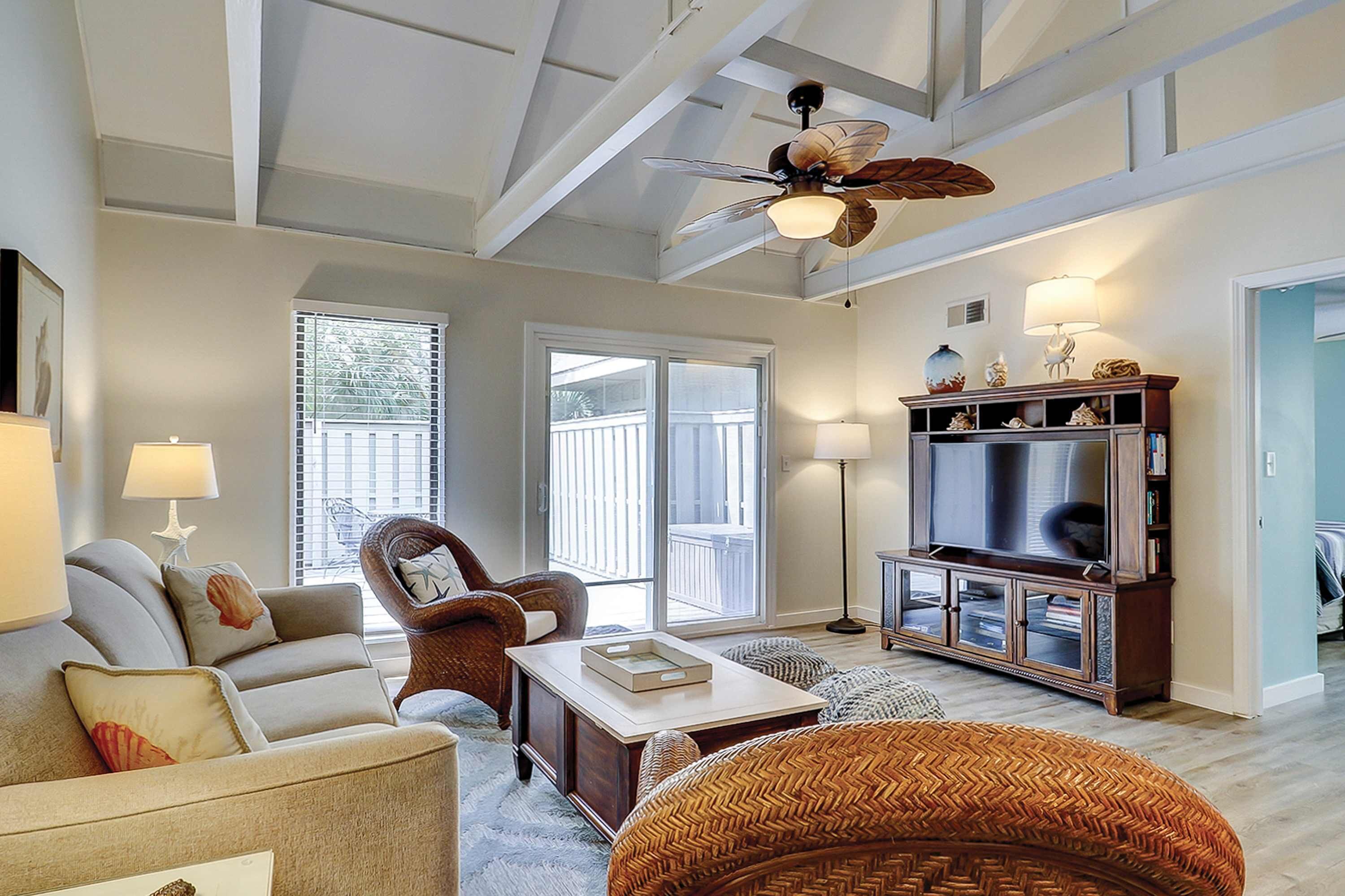 A spacious living room with a high ceiling, a ceiling fan, a television, and a comfortable seating area with a sofa and chairs.