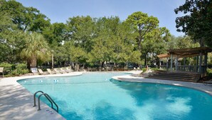 Una piscina con cubierta de madera, sillas de descanso y una zona de estar techada.
