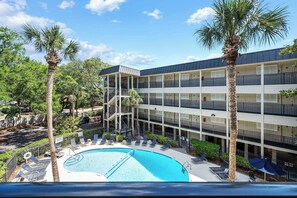 A multi-story hotel with a swimming pool, palm trees, and a covered outdoor area. - Stunning Newly Renovated Condo with Ocean View & Shared Pool Close to the Beach (Hilton Head)