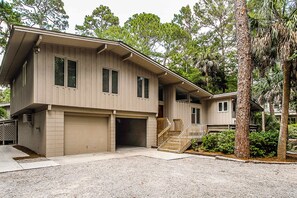 A two-story house with a garage, a covered porch, and a staircase leading to the second floor. - Secluded home & pool house with private pool - steps away from the beach (Hilton Head)