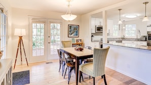 A dining area with a wooden table and chairs, a pendant light, and a view of the kitchen. - Relaxing Evian villa with patio, pool, tennis, pickleball, beach, golf, Dogs ok (Hilton Head)