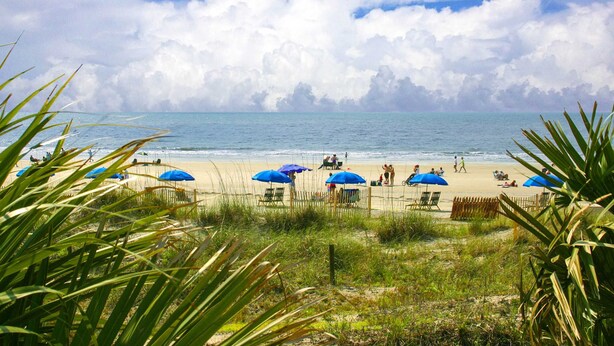 A beach with umbrellas, people, and a fence. - Relaxing Evian villa with patio, pool, tennis, pickleball, beach, golf, Dogs ok (Hilton Head)