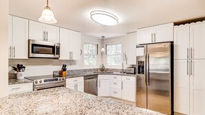 A kitchen with white cabinets, stainless steel appliances, granite countertops, and a large island. - Relaxing Evian villa with patio, pool, tennis, pickleball, beach, golf, Dogs ok (Hilton Head)