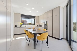 A modern kitchen with a dining area, large windows, and a view of the outside. - Villa - Casa Nunca Desista (Atalaia)