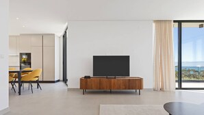 Ein modernes Wohnzimmer mit Flachbildfernseher, einem Essbereich mit gelben Stühlen und einem großen Fenster mit Blick.