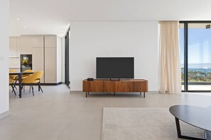 A modern living room with a flat-screen TV, a dining area with yellow chairs, and a large window with a view. - Villa - Casa Nunca Desista (Atalaia)