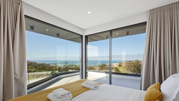 Ein modernes Schlafzimmer mit einem großen Bett, Meerblick und einem Balkon.