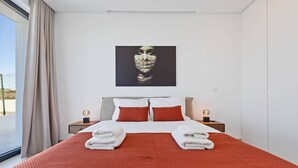Ein modernes Hotelzimmer mit einem großen Bett, zwei Nachttischen mit Lampen, einem Fenster mit Vorhängen und einem Wandbild.