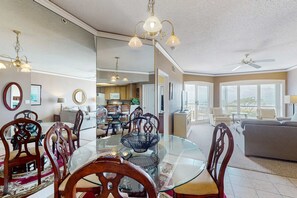 A spacious living area with a dining table, chairs, and a ceiling fan. - Island getaway by the ocean with balcony view & shared pool and beach access (Hilton Head)