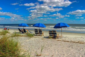 A beach with chairs and blue umbrellas, a sandy shore, and the ocean in the background. - Beautiful Home On George Fazio Golf Course Close to the Beach (Hilton Head)