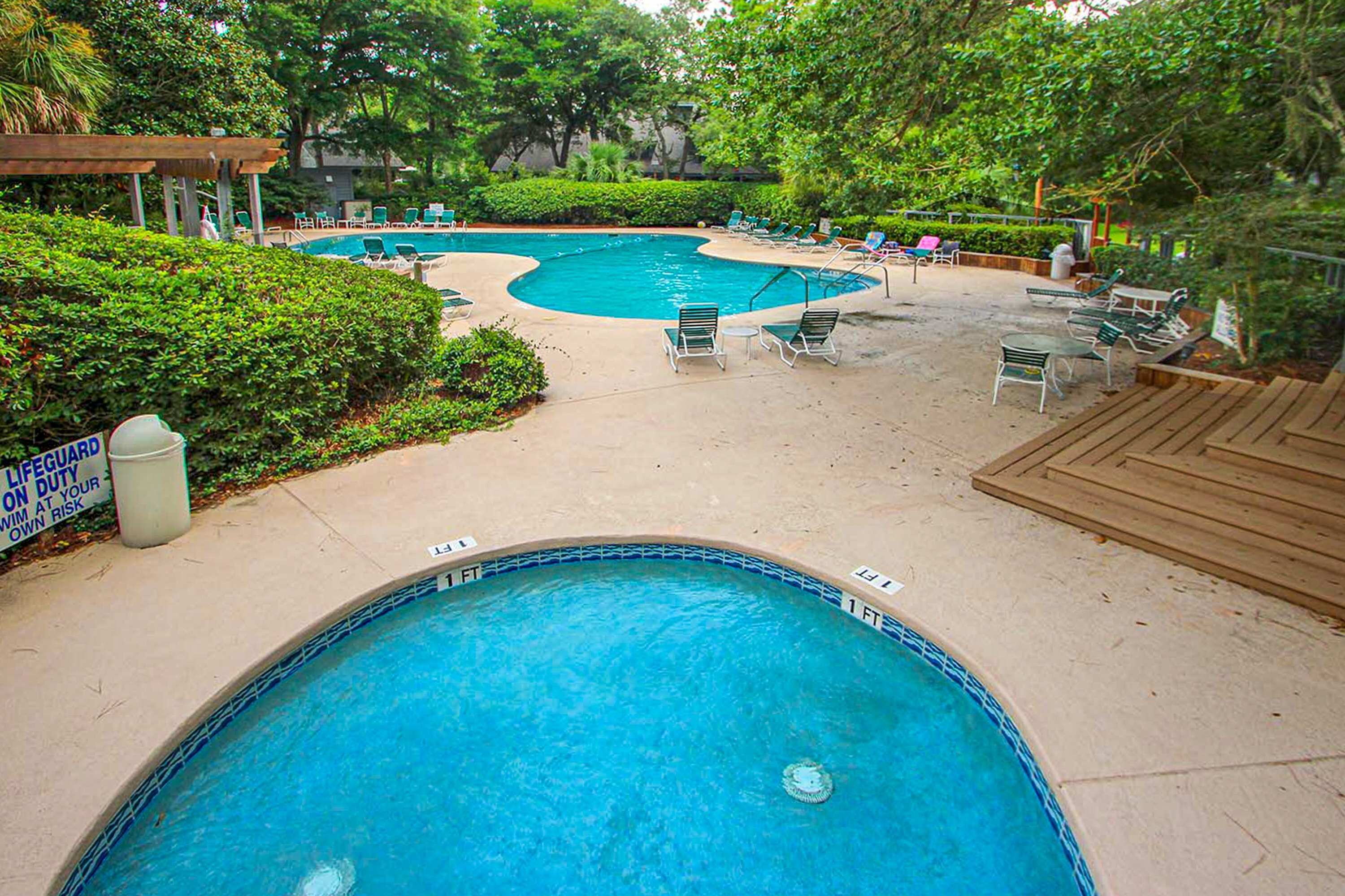 A swimming pool with lounge chairs and a lifeguard on duty sign.