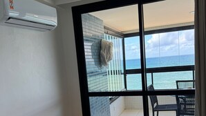 Een kamer met een bed, een bureau en uitzicht op de oceaan door een schuifdeur.