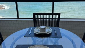 Een eettafel met borden, bekers en bestek, geplaatst op een glazen tafel met uitzicht op de oceaan.
