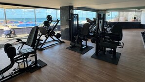 Een fitnessruimte met cardiotoestellen, gewichten en uitzicht op het strand.