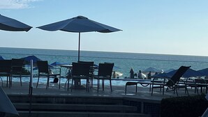 Zwembadgedeelte met stoelen en parasols, met uitzicht op de zee.