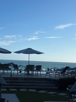 A poolside area with chairs and umbrellas, overlooking the sea. - Beachfront Apartment (Salvador)