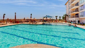 A swimming pool with lounge chairs and umbrellas, surrounded by palm trees and a multi-story building. - Sunny condo with ocean view balcony & beach access (Hilton Head)