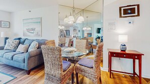 A living room with a sofa, wicker chairs, a glass dining table, and a wooden side table. - Sunny condo with ocean view balcony & beach access (Hilton Head)