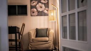 Una habitación con un sillón color crema, una lámpara de pie, un estante en la pared y un suelo estampado.
