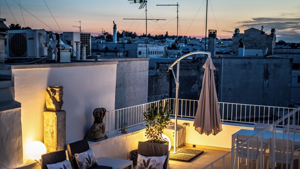 Una terraza en la azotea con mobiliario exterior, una planta en maceta y una estatua.