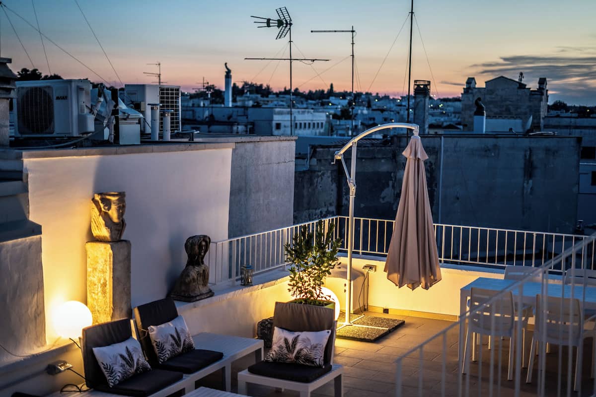 A rooftop terrace with outdoor seating, a potted plant, and a statue.