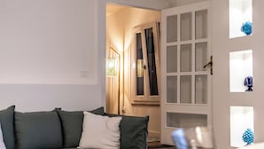 Un salón con un sofá verde, una puerta blanca con paneles de vidrio y una pequeña mesa con adornos.
