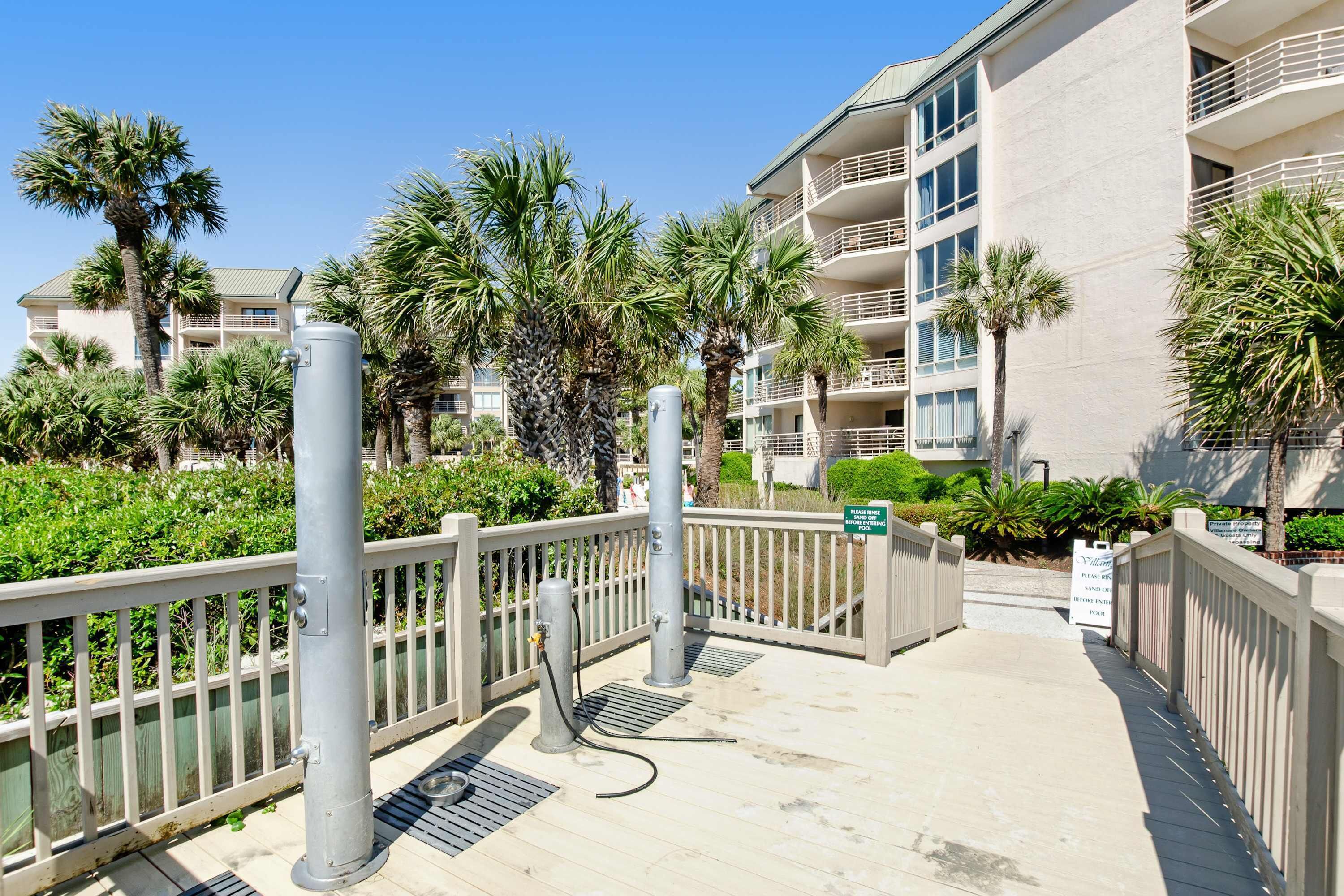 A gated entrance to a building with a palm tree-lined pathway, a sign indicating a valet parking area, and a clear blue sky.