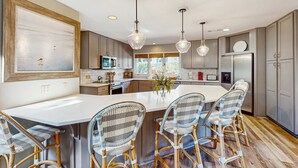 A modern kitchen with a large island, wicker chairs, pendant lights, and built-in appliances. - Fully Renovated Sea Pines Home w Private Pool Six Rows from the Water  Dogs OK (Hilton Head)