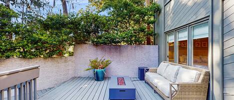 A deck with a wicker sofa, a blue planter, and a small table.