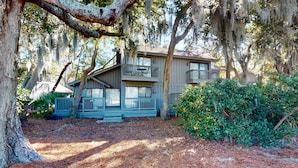 A two-story building with a balcony, surrounded by trees and a wooden deck. - Sunny getaway with full kitchen, furnished deck, and shared pool (Hilton Head)