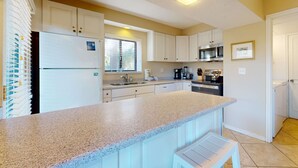 A kitchen with white cabinets, a granite countertop, a refrigerator, a microwave, and a coffee maker. - Sunny getaway with full kitchen, furnished deck, and shared pool (Hilton Head)