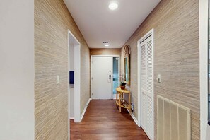 A hallway with wooden panel walls, a white door at the end, and a small wooden table with a plant. - Condo with soaring ceilings, a deck, lagoon views, & shared tennis (Hilton Head)