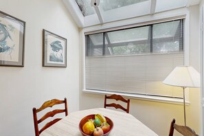A dining area with a table, chairs, a bowl of fruit, and a window with blinds. - Condo with soaring ceilings, a deck, lagoon views, & shared tennis (Hilton Head)