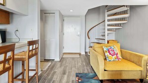 Un saló modern amb un sofà, cadires de fusta, una escala i una porta que dona a una altra habitació.