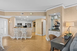 A modern kitchen with white cabinets, a central island with bar stools, and a dining area with a table and chairs. - Bright & Airy Retreat with Balcony Views, Walkable Beach Access & Central Location (Hilton Head)