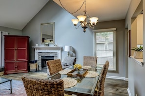A dining area with wicker chairs, a glass table, and a chandelier. - Bright and inviting condo with shared pools & tennis courts near the beach (Hilton Head)