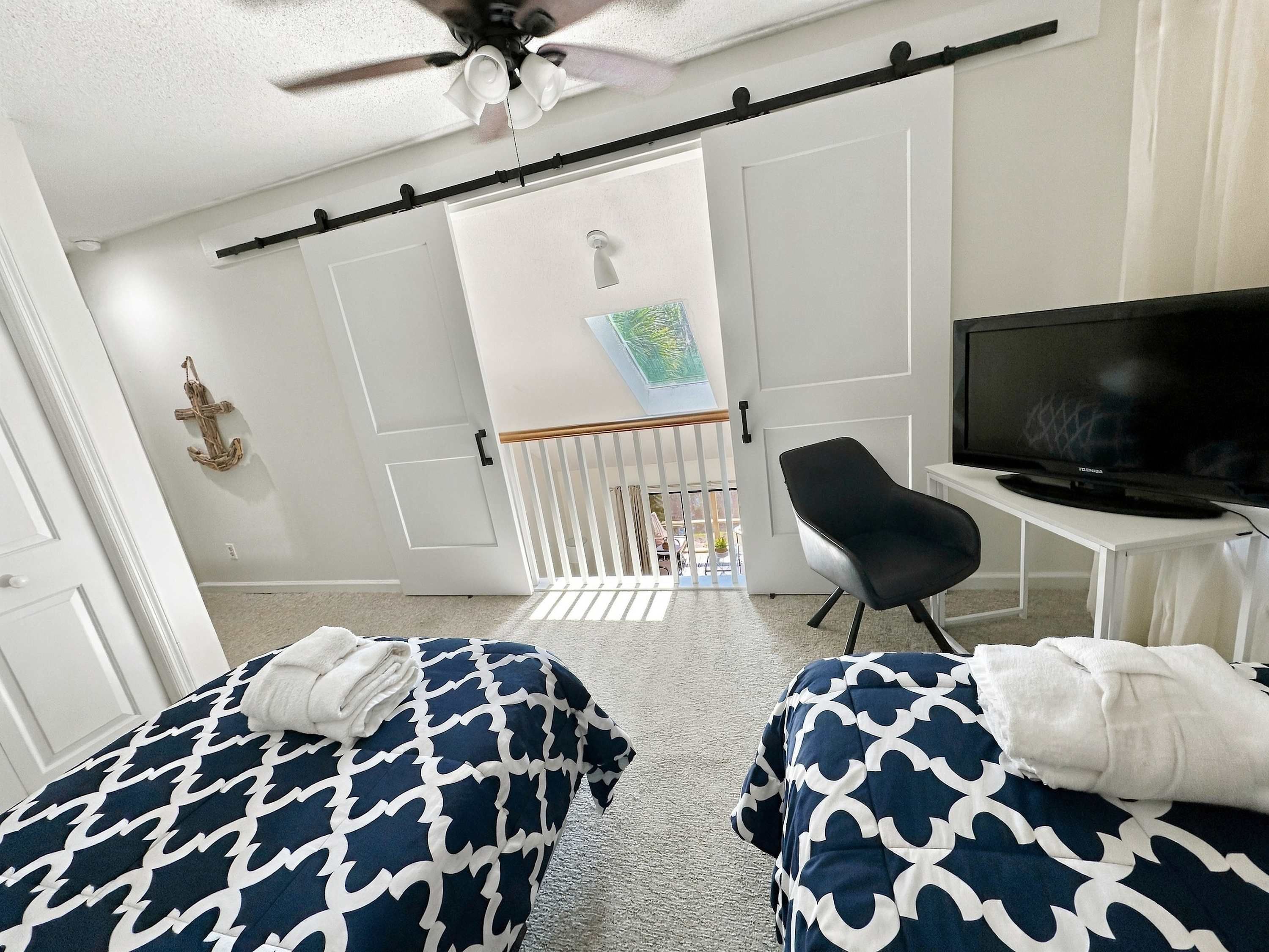 Una habitación con una cama, una silla, un televisor y un ventilador de techo.