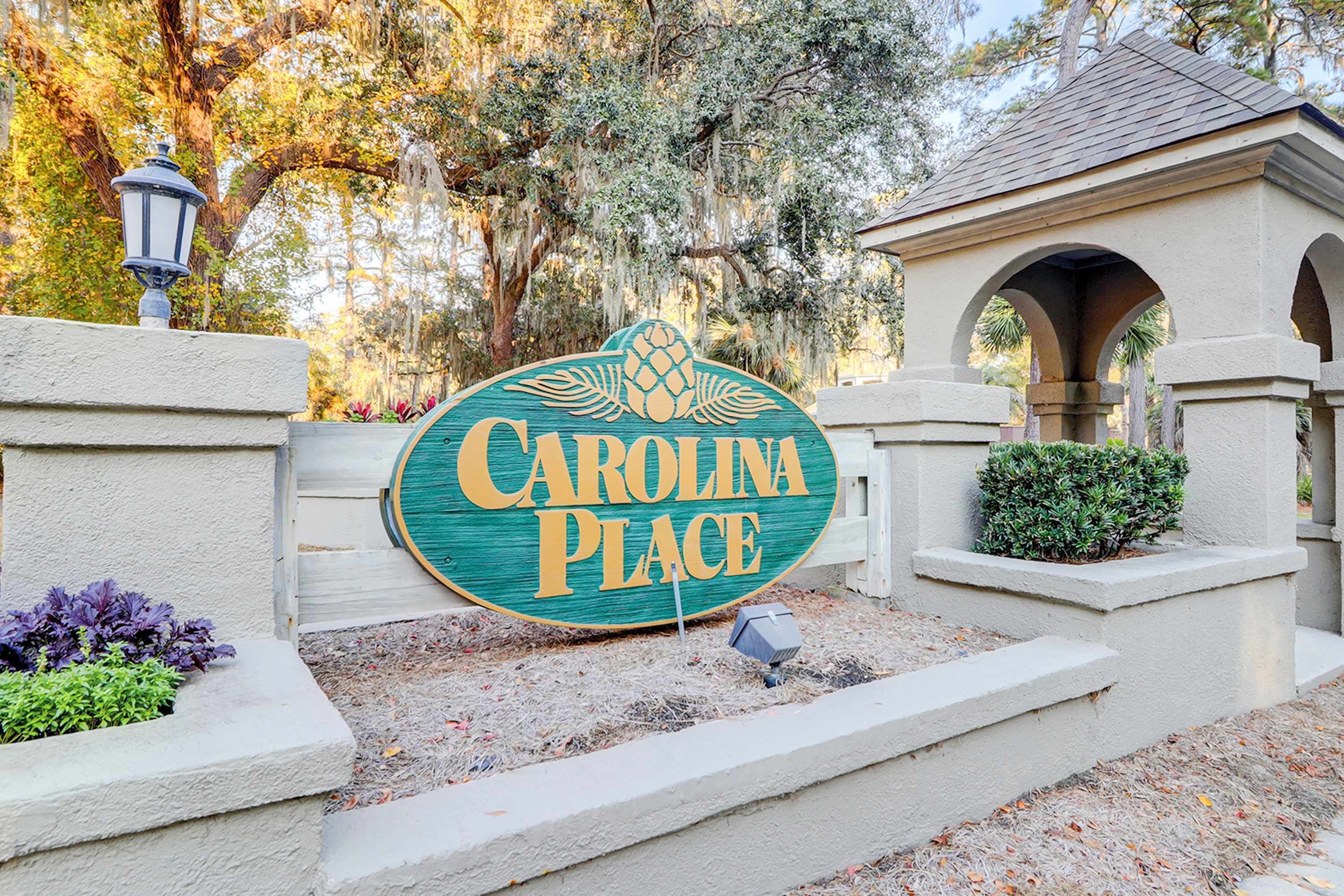 A sign for Carolina Place with a stone wall and a lamp post.