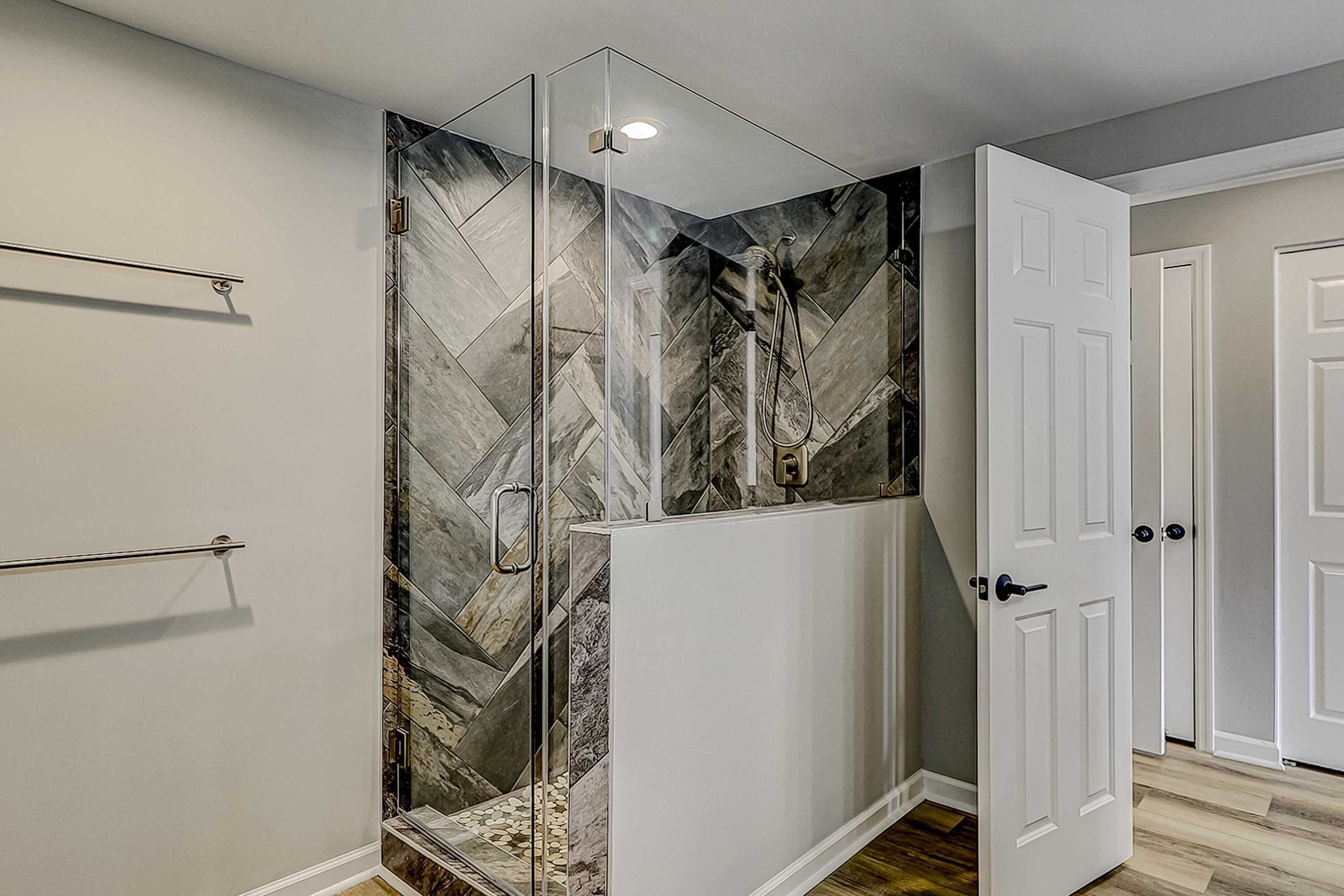 A shower with a glass enclosure and a herringbone tile pattern on the walls.