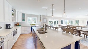 Une cuisine moderne avec des meubles blancs, un grand îlot central doté d’un évier et des luminaires suspendus.