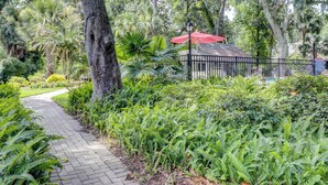 Un camino que lleva a un edificio con un paraguas rojo, rodeado de exuberante vegetación y árboles.
