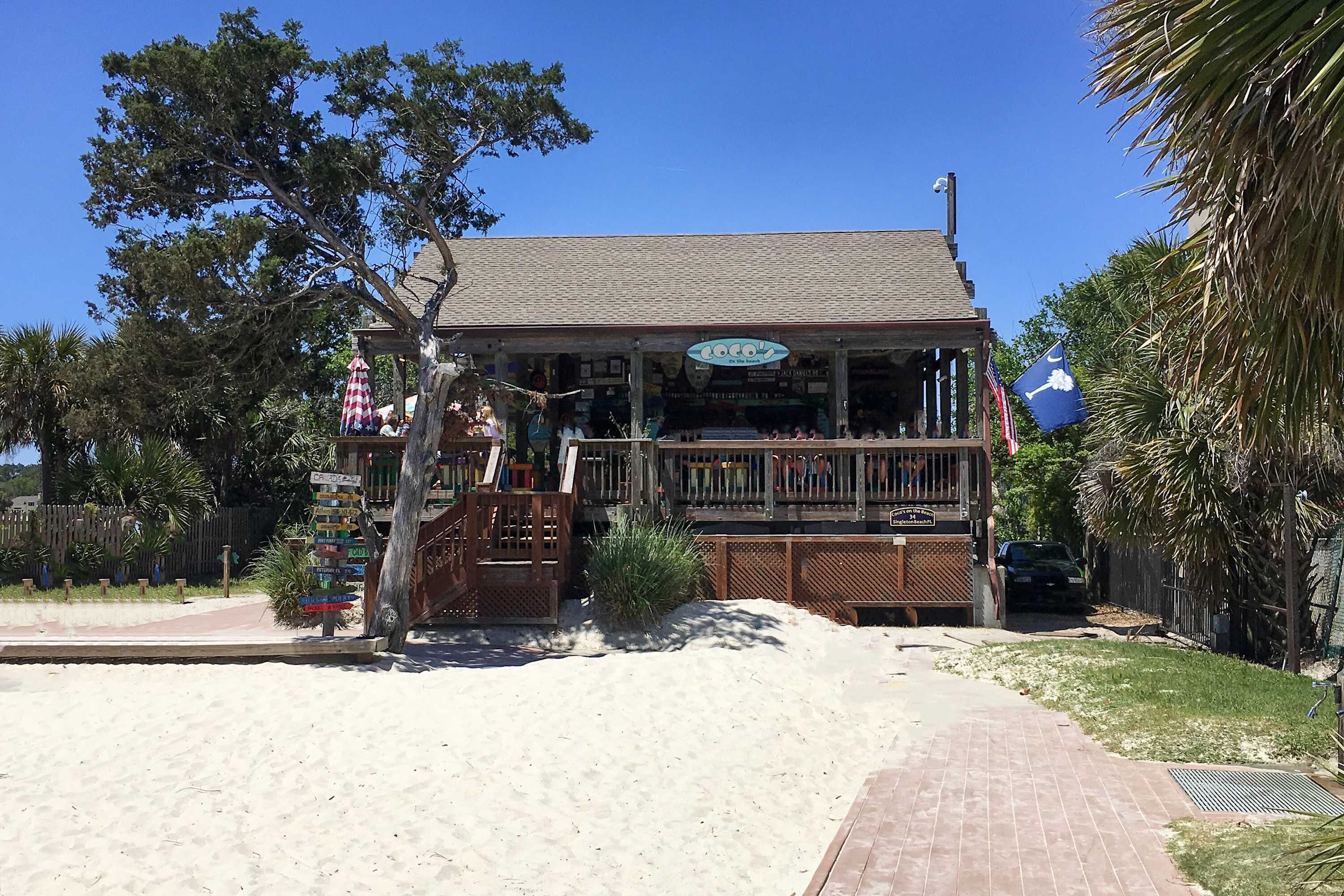 A beachfront building with a signboard, a wooden deck, and a sandy area in front.